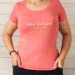 half body photo of a woman in a pink t-shirt with embroidered text.