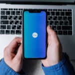 hand holding a phone with a Canva logo over a laptop.